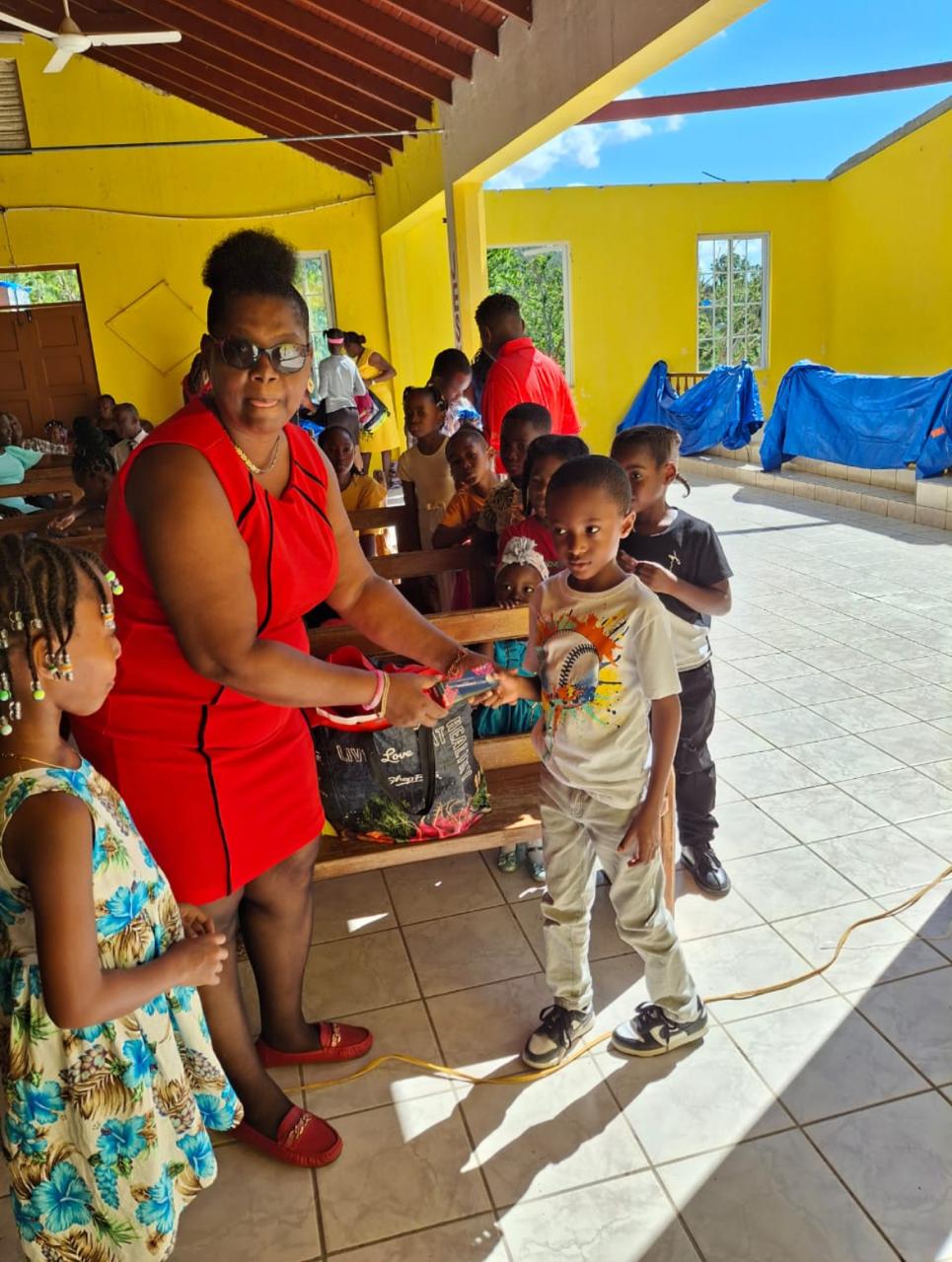 A woman in a red dress hands a gift to a young boy in a casual shirt during a colorful community event for children.