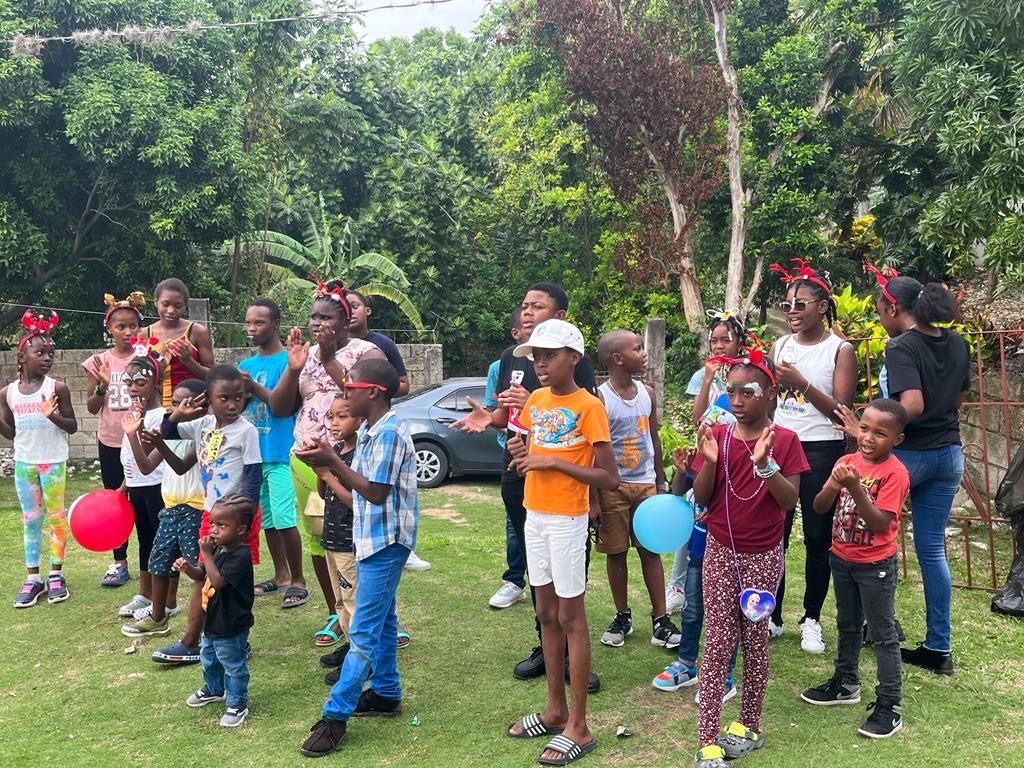 Children wearing festive attire celebrate together outdoors, joyfully singing and playing with balloons during a lively gathering.