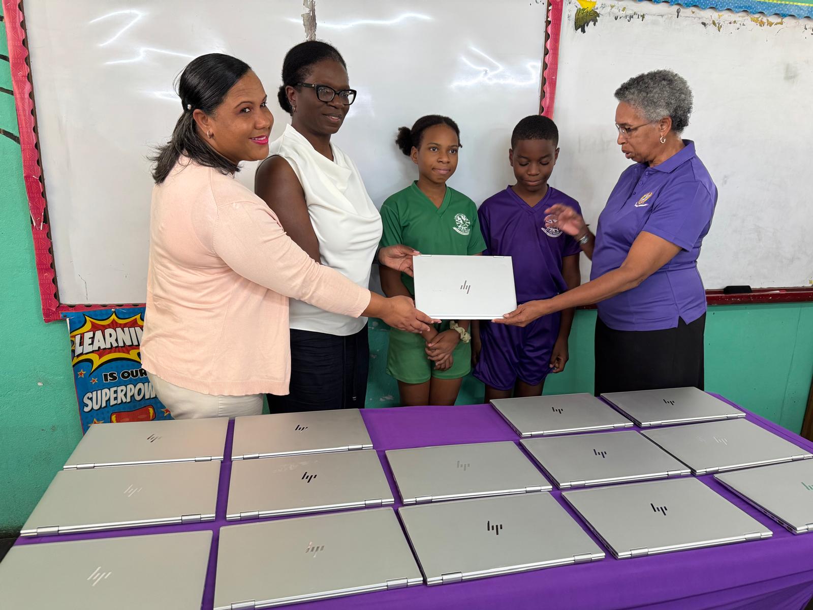 Donation event in a classroom showing four individuals presenting laptops to two students, highlighting educational support and technology access.