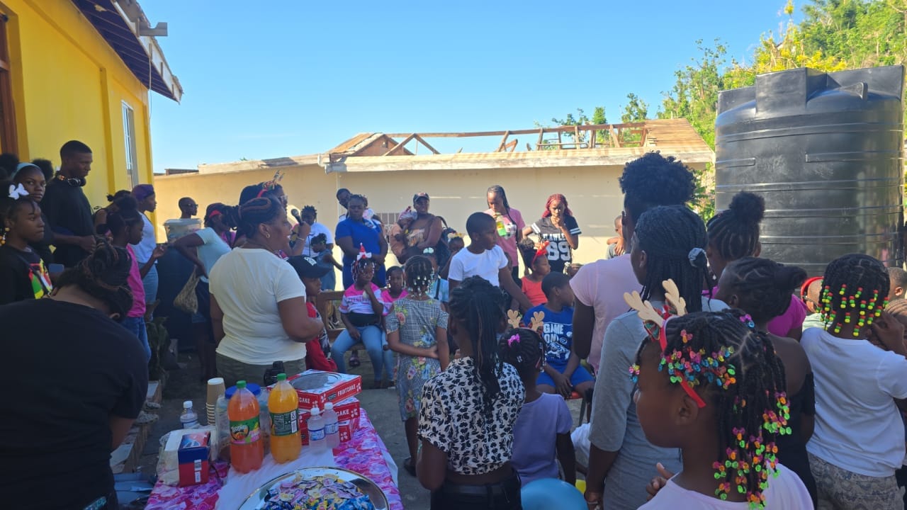 A lively outdoor gathering of children and adults enjoying a festive celebration, with colorful decorations, snacks, and drinks visible on a table.