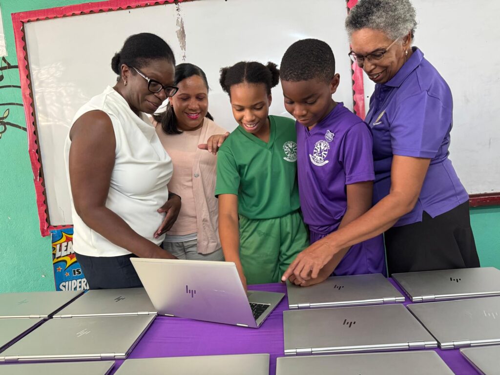 Students and educators gather around a laptop, exploring technology together, highlighting collaborative learning in an educational setting.
