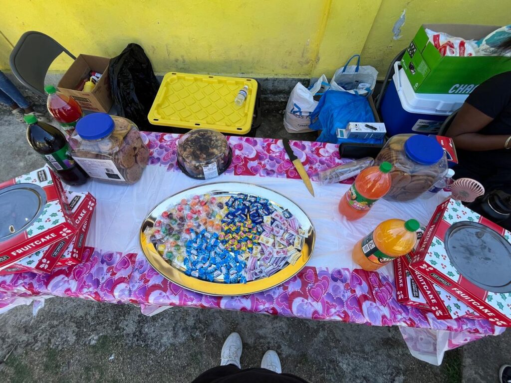 Colorful assortment of candies, fruitcakes, snacks, and drinks arranged on a table with a pink floral tablecloth, set for a festive gathering.