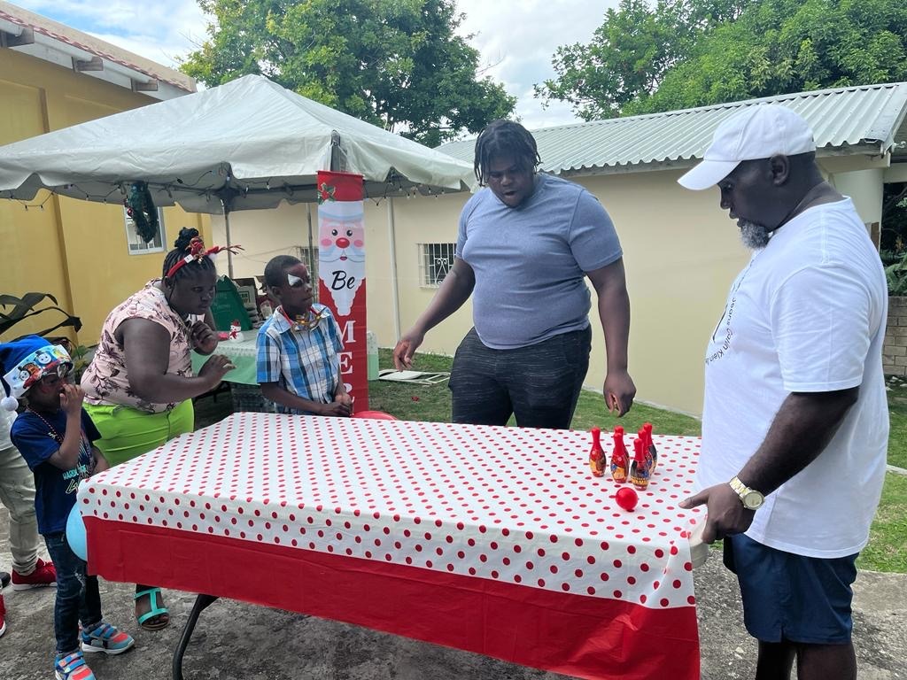 Family gathering featuring adults and children engaging in a game around a table decorated with a polka-dot tablecloth and colorful bottles.