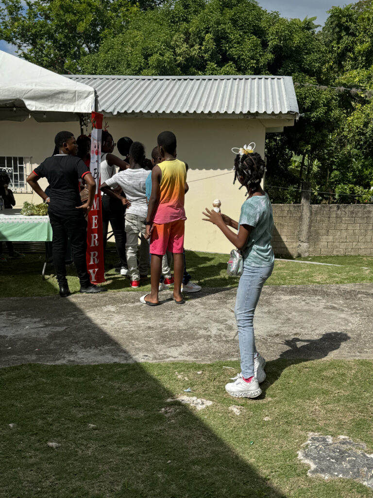 Children gather under a tent at an outdoor event. One girl in the foreground holds an ice cream cone, while others line up behind her.