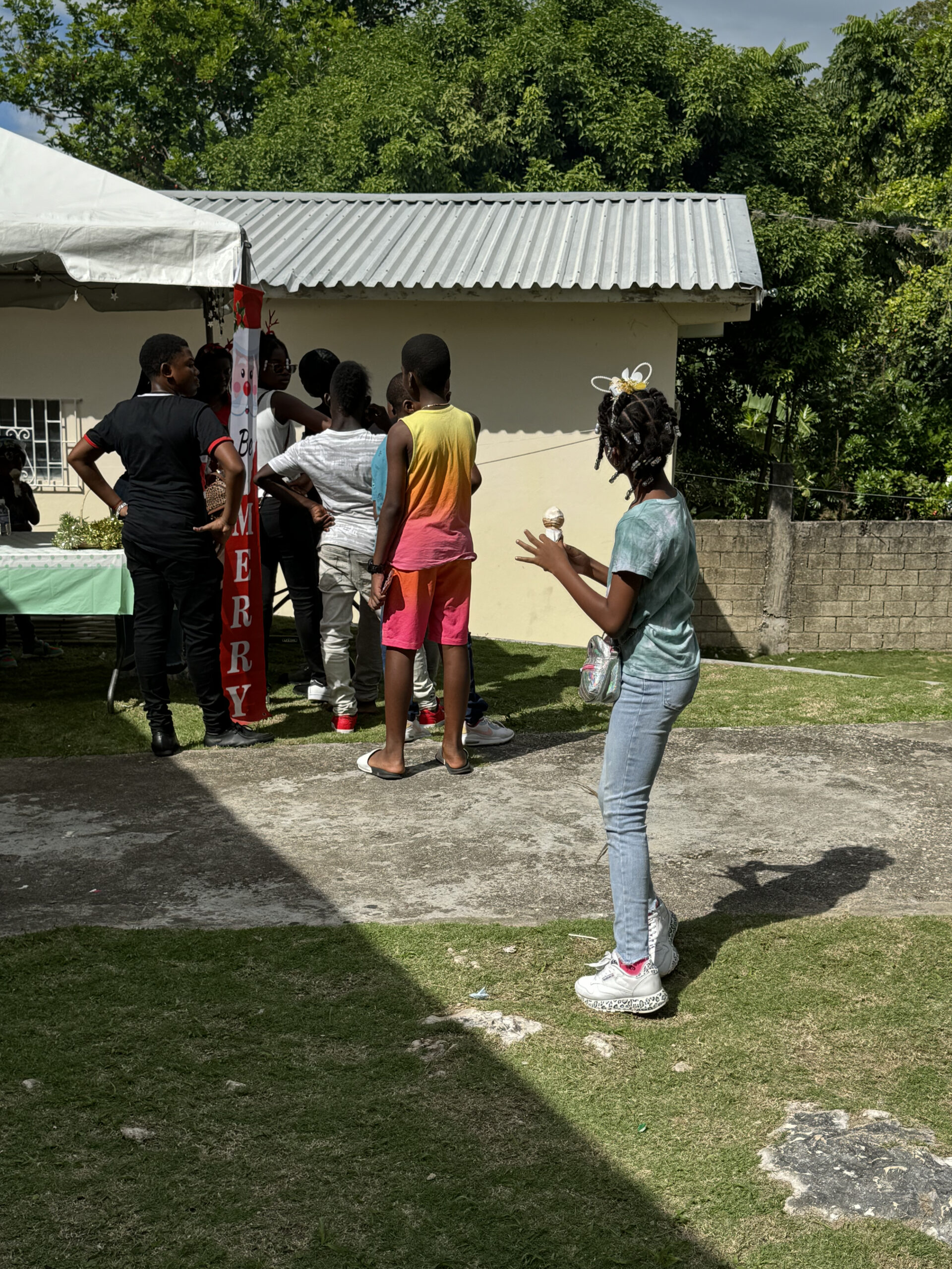 Children gather under a tent at an outdoor event. One girl in the foreground holds an ice cream cone, while others line up behind her.