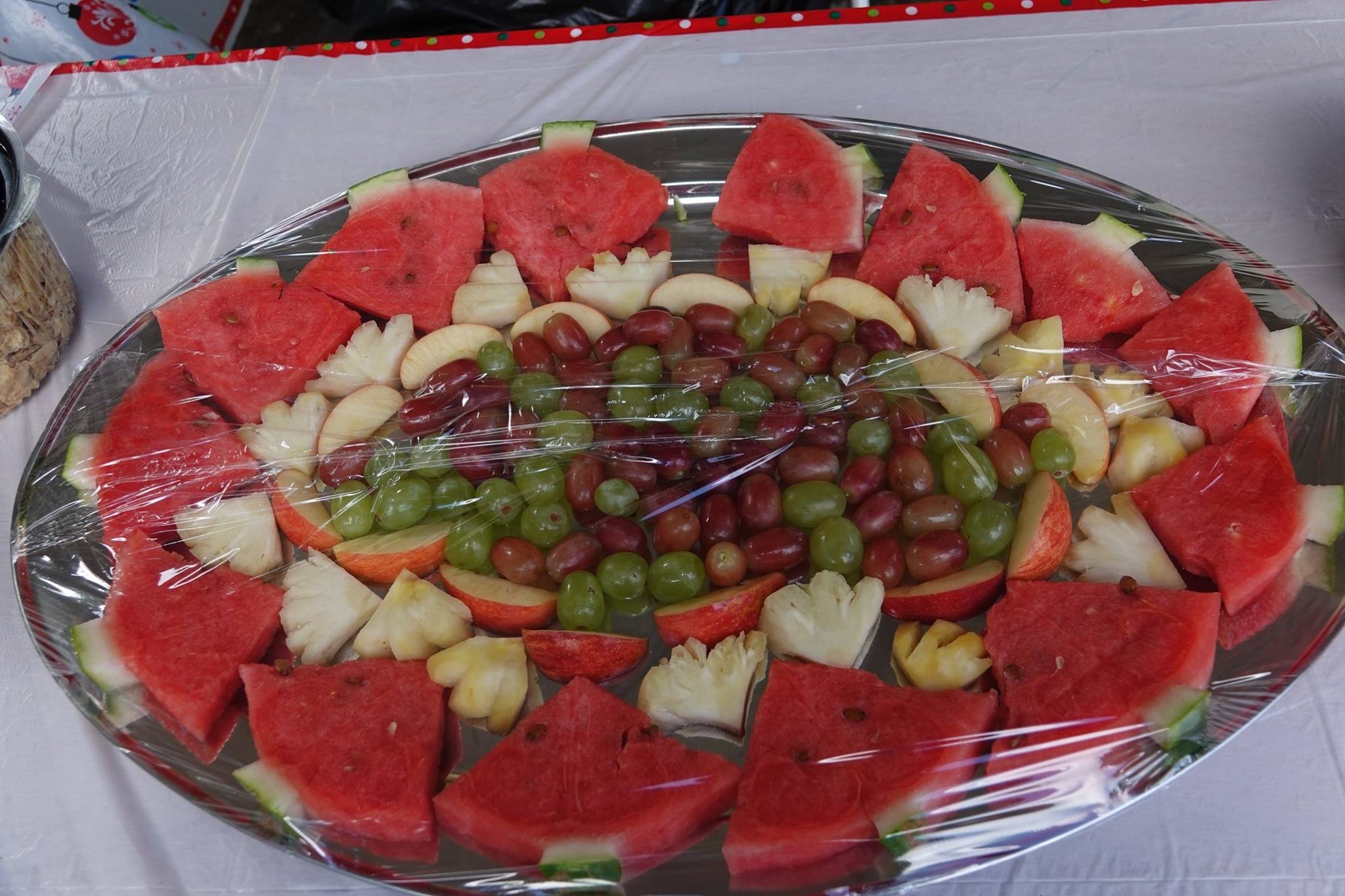Colorful fruit platter featuring slices of watermelon, pineapple, and assorted grapes. Wrapped in plastic, it serves as a refreshing snack option.