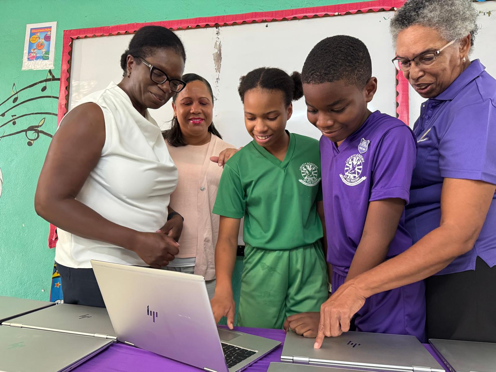 Students and educators engage around laptops in a classroom, highlighting collaboration and learning through technology.